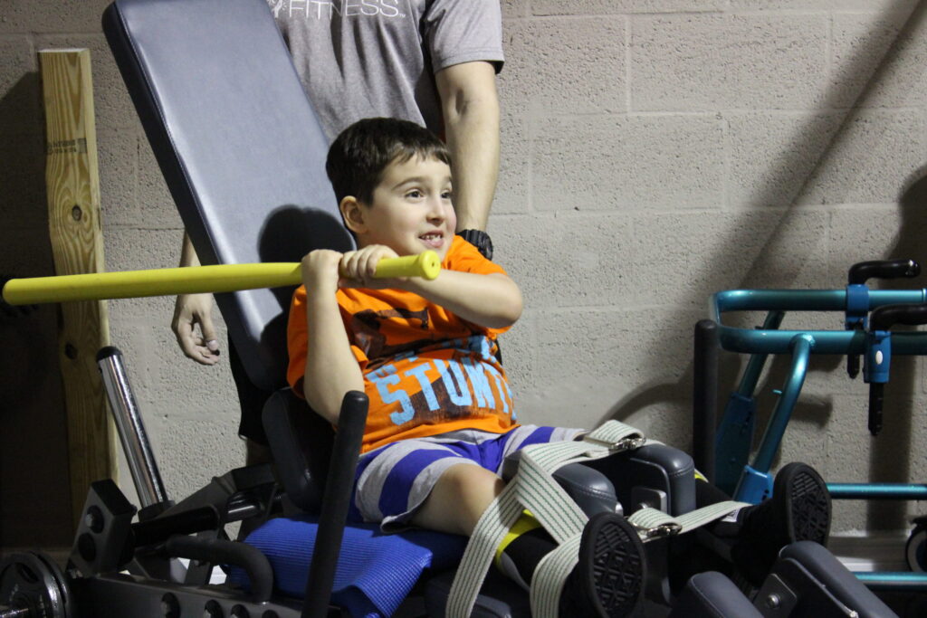 A young boy in a standing frame gripping a bar during therapy