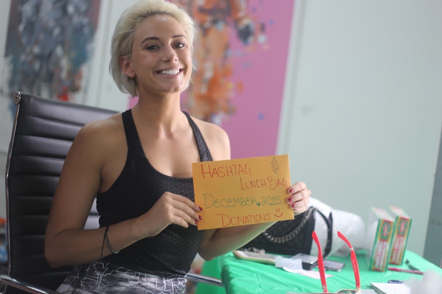 YesJulz smiling and holding a handwritten cardboard sign at a table