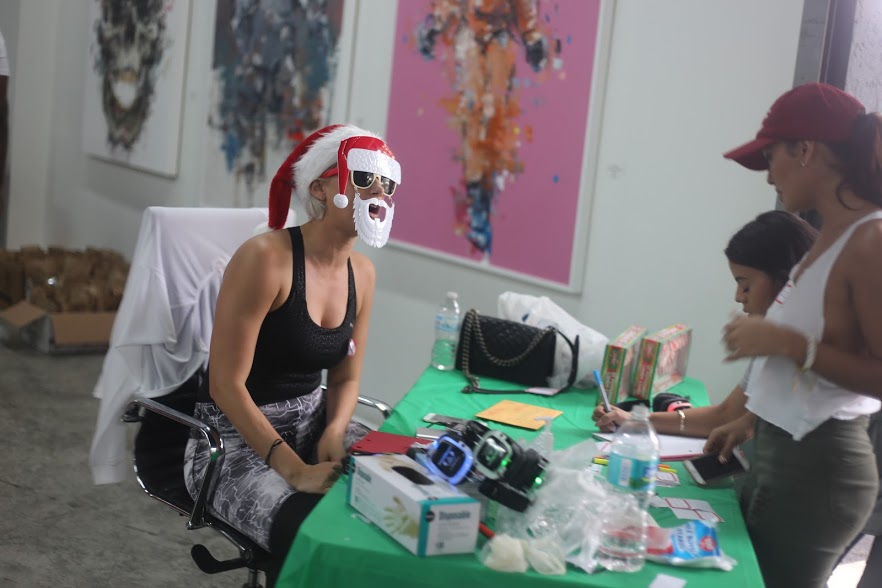 A woman in a Santa beard at a table sorting donations with a volunteer