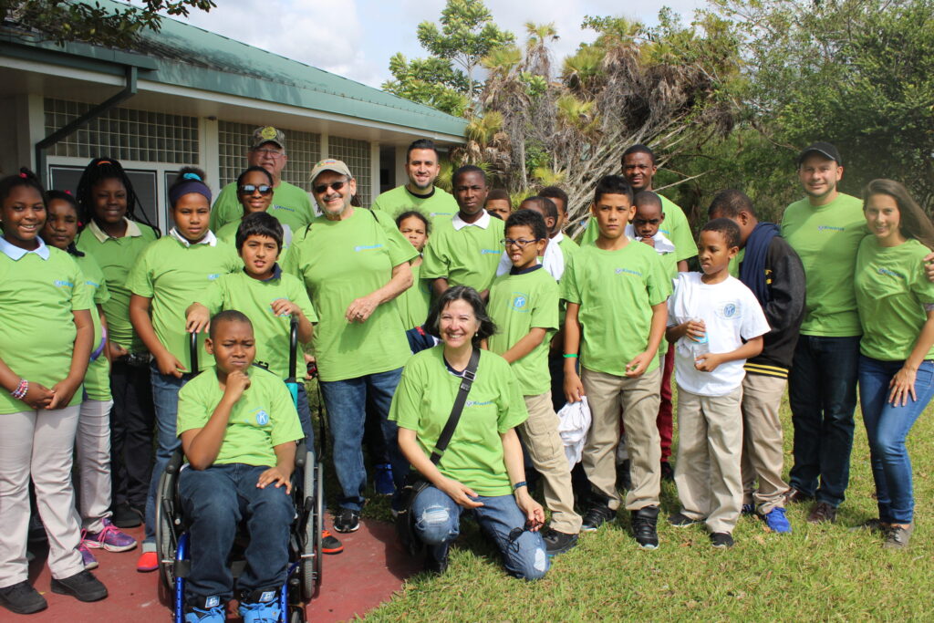 A group of fourth-graders and adults in green T-shirts posing outside a building