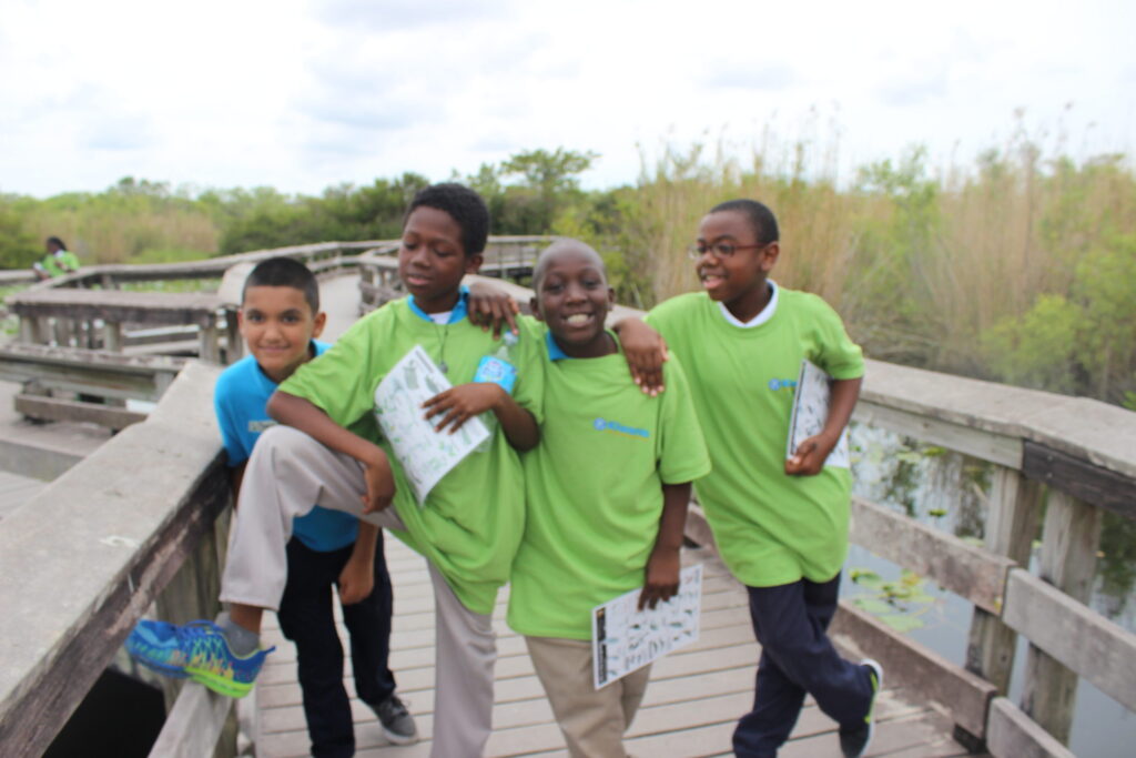 Four boys in green T-shirts walking arm in arm along a boardwalk