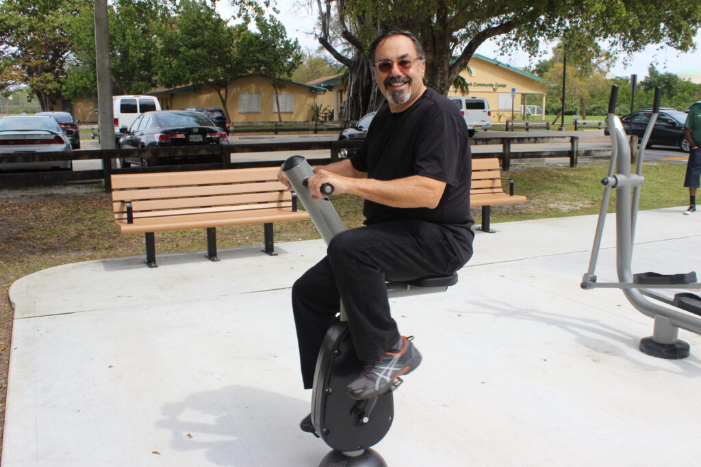 A man in black using a seated exercise machine in a park