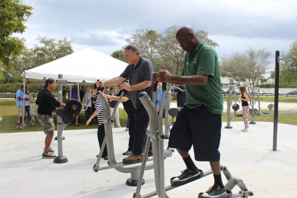 People trying out new outdoor fitness equipment under a white tent in a park