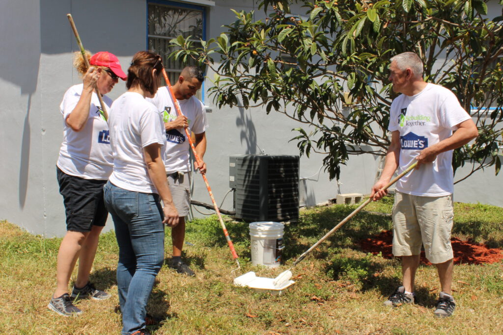 Volunteers in matching T-shirts painting and clearing a yard with long rollers