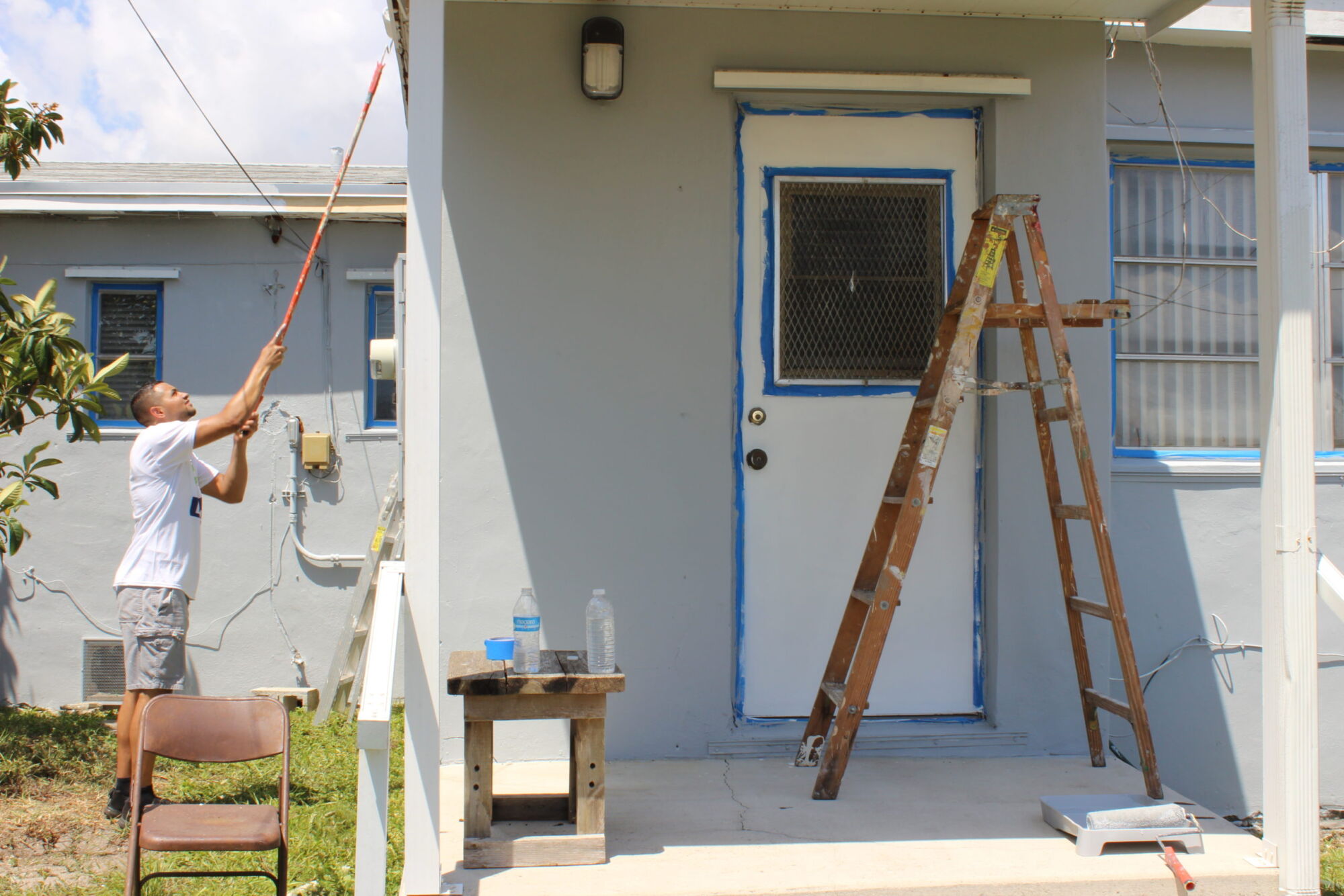 A volunteer painting the eaves of a white house with a long roller