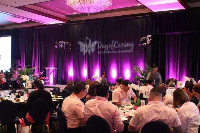 Guests at round tables in a ballroom lit purple, a Day of Caring banner on stage