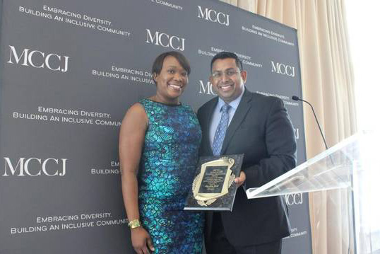 Joy Reid and a man holding an award plaque in front of an MCCJ backdrop