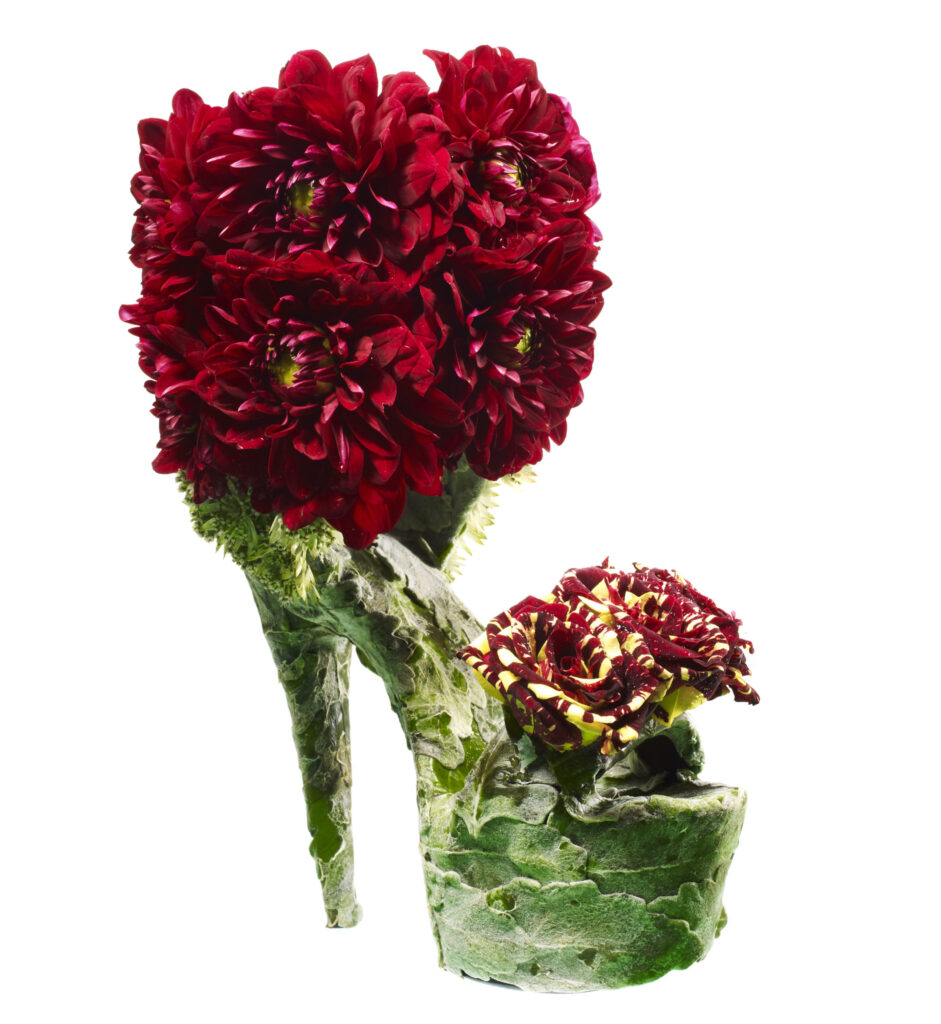 A high-heeled shoe sculpture made of red flowers and green leaves