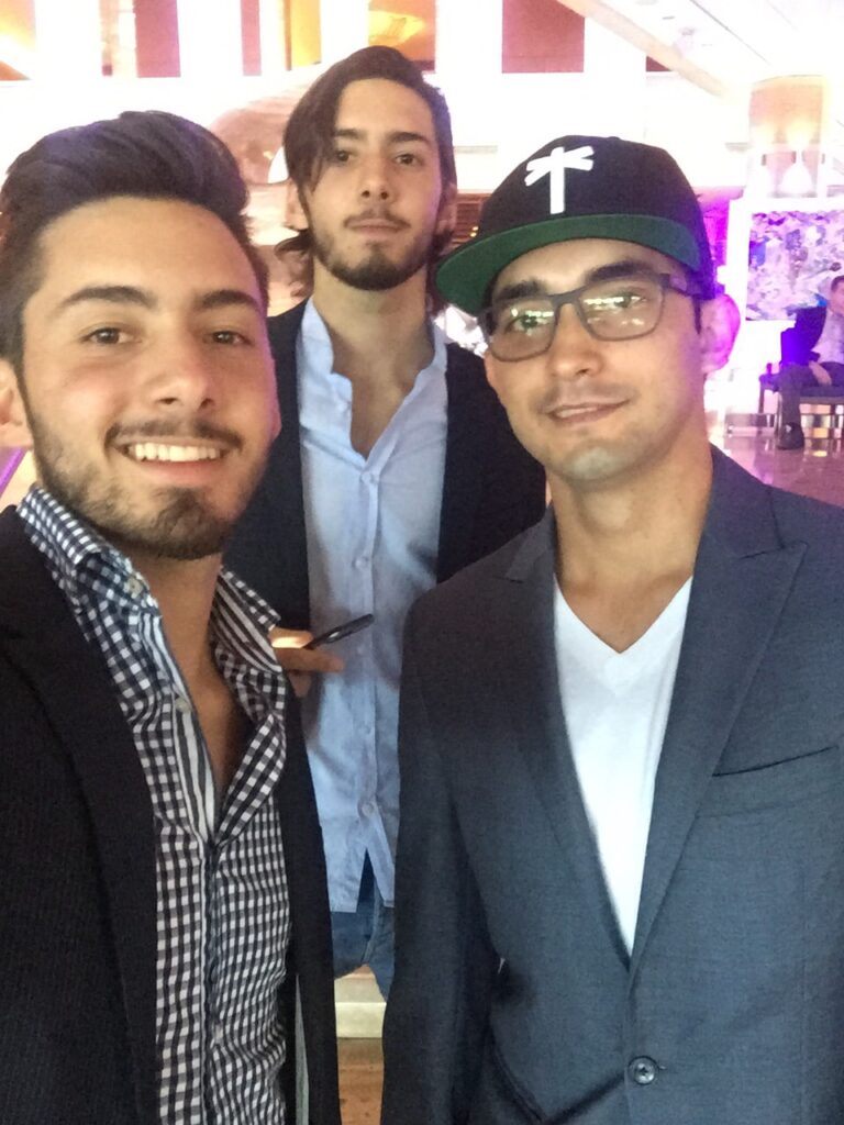Three young men, one in a cap, posing for a selfie at an event