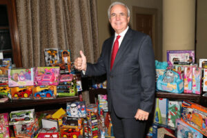 Carlos Giménez giving a thumbs up beside shelves of donated toys