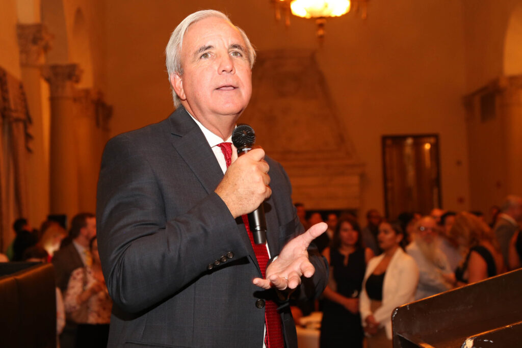 Carlos Giménez speaking into a microphone to a crowd in a grand hall