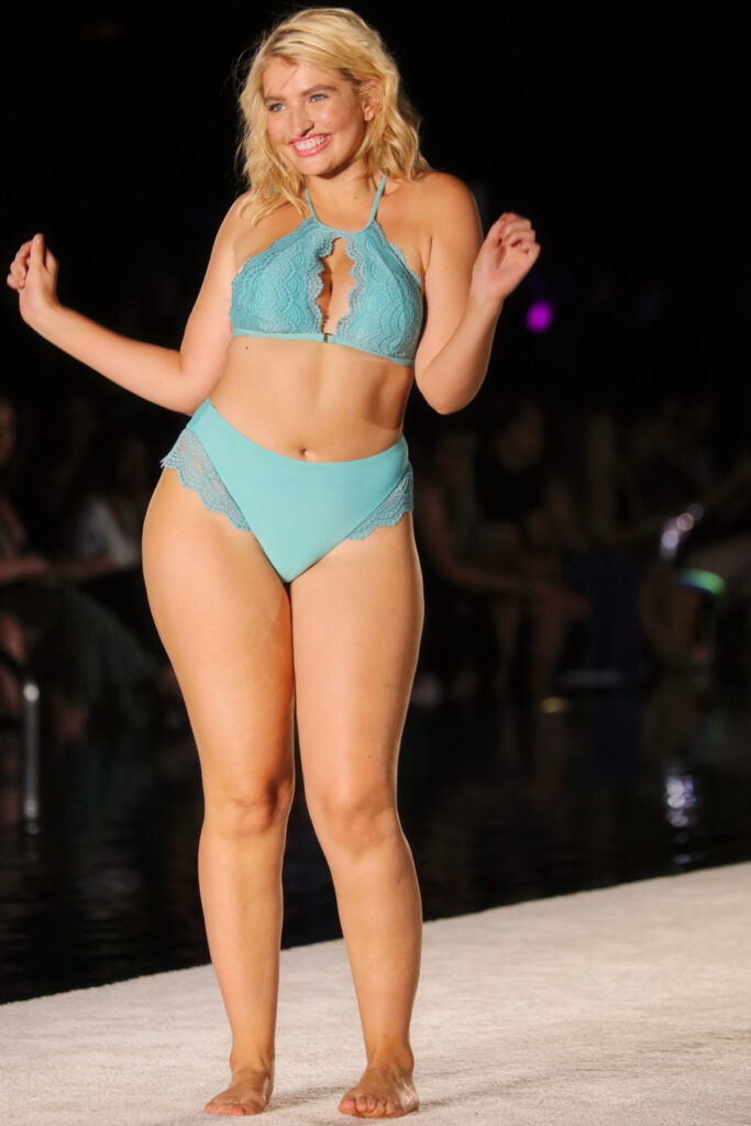 A model in a turquoise halter bikini dancing on a Swim Week runway