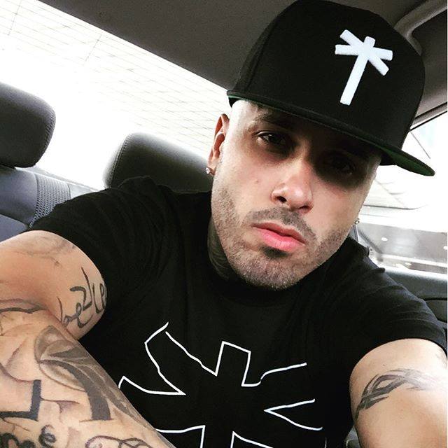 Nicky Jam in a black cap and Palm Era T-shirt taking a selfie in a car