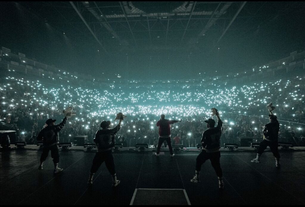 Performers on stage facing an arena full of phone lights in the dark
