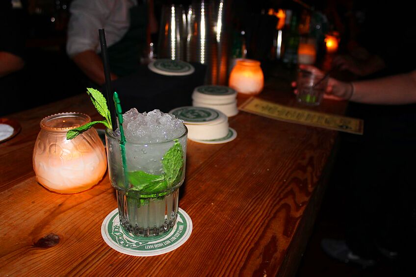 A mojito with fresh mint on a wooden bar beside a candle
