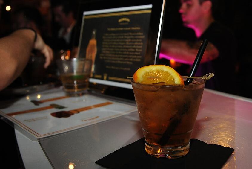 A cocktail with an orange slice on a bar beside a printed menu