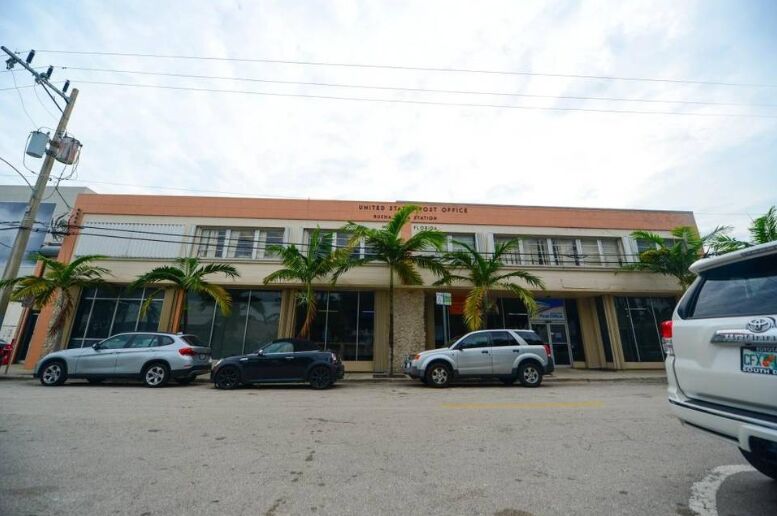 A low post office building with cars parked in front and palm trees