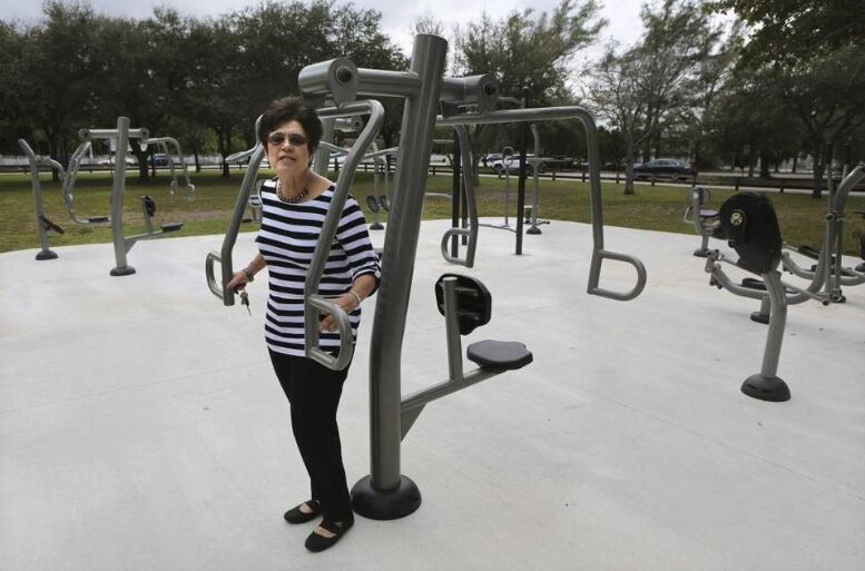 A woman in a striped top using outdoor fitness equipment in a park