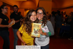 Two girls smiling and holding up a copy of Harry Potter and the Cursed Child
