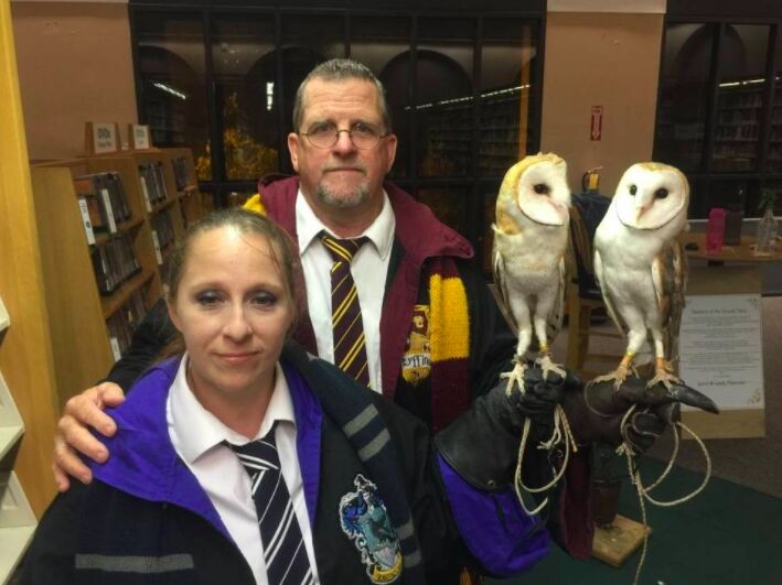 Two people in Hogwarts robes and ties with two barn owls perched on a handler's glove