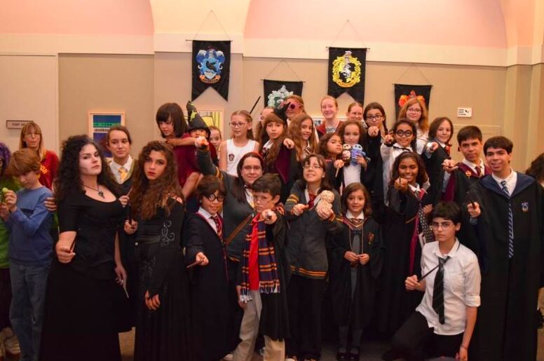 A crowd of Harry Potter fans in robes and house scarves posing under house banners in a library
