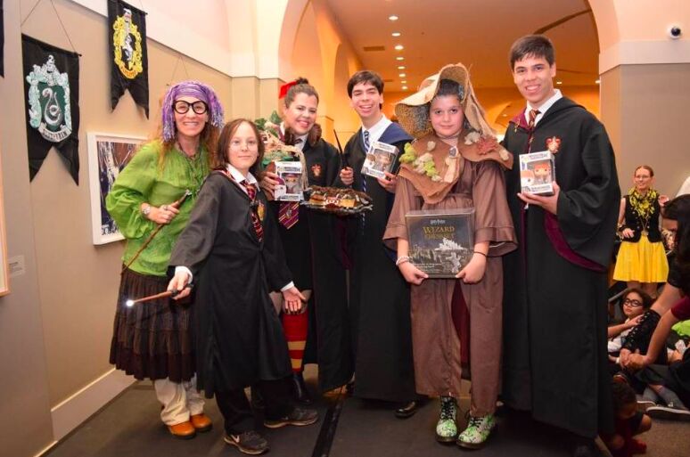Fans in Harry Potter costumes, one holding a book, standing in front of house banners