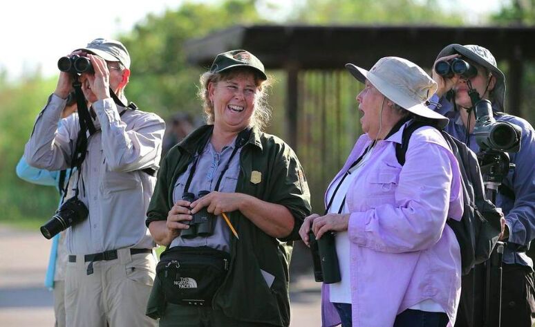 Birdwatchers with binoculars and cameras laughing together with a park ranger
