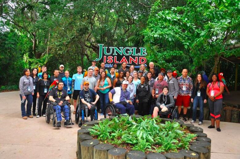 A large group of wounded veterans and supporters, some in wheelchairs, in front of the Jungle Island sign