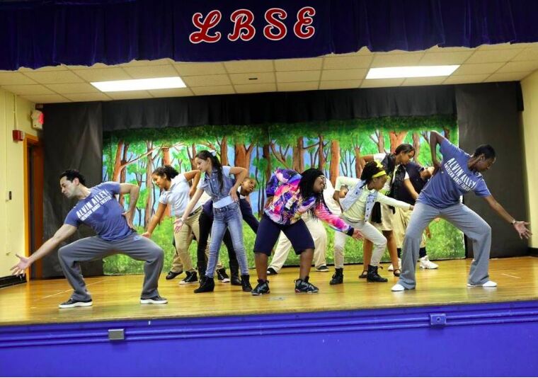 Children dancing in a line on a school stage in front of a painted jungle backdrop