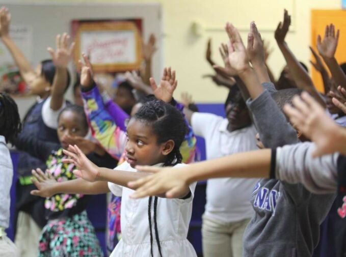 Children stretching their arms out in a crowded school dance class