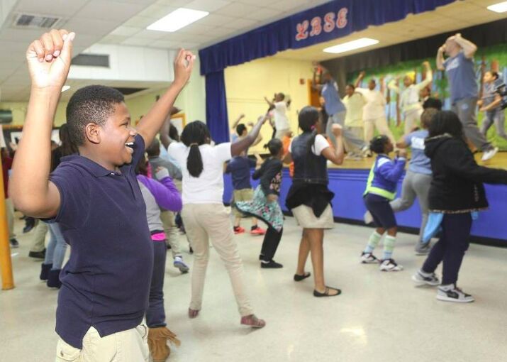 A boy raising his arm with a big smile in a school gym dance class