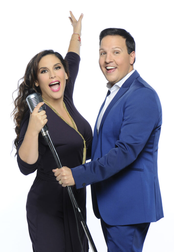 Angélica Vale holding a vintage microphone beside Raúl González in a blue suit
