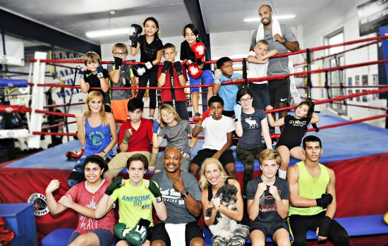 A large group of children and adults in boxing gloves posing in and around a boxing ring