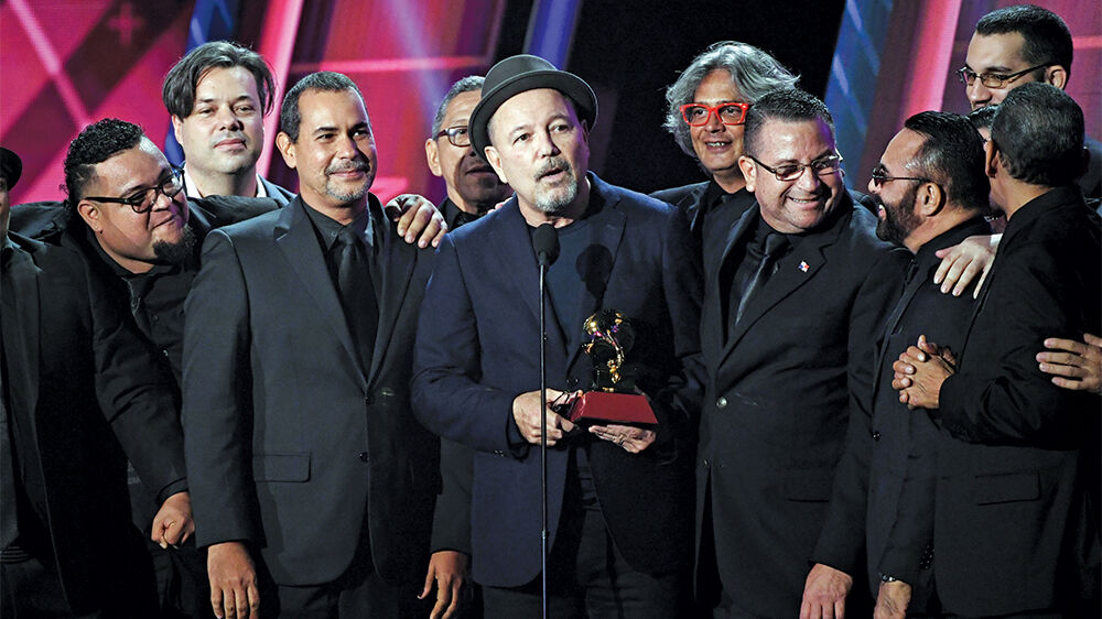 Rubén Blades and a large band in black holding a Latin Grammy on stage