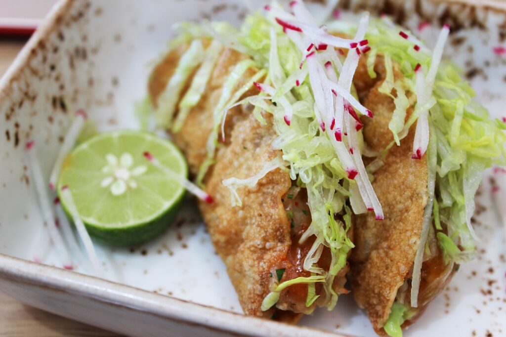Fish tacos topped with shredded cabbage and radish, with a lime half
