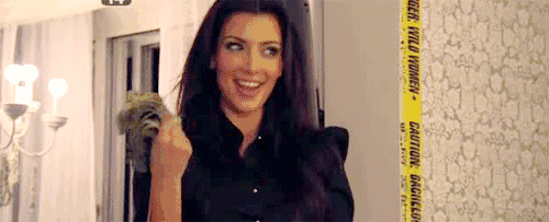 Kim Kardashian smiling in a black shirt, holding up a wad of cash