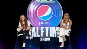 Shakira and Jennifer Lopez sitting on stage at a Pepsi Super Bowl Halftime Show press conference