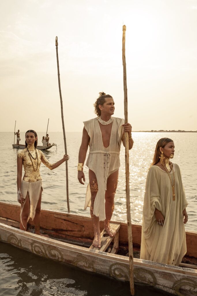 Two women in white standing in a wooden canoe at sunset, one holding a long pole