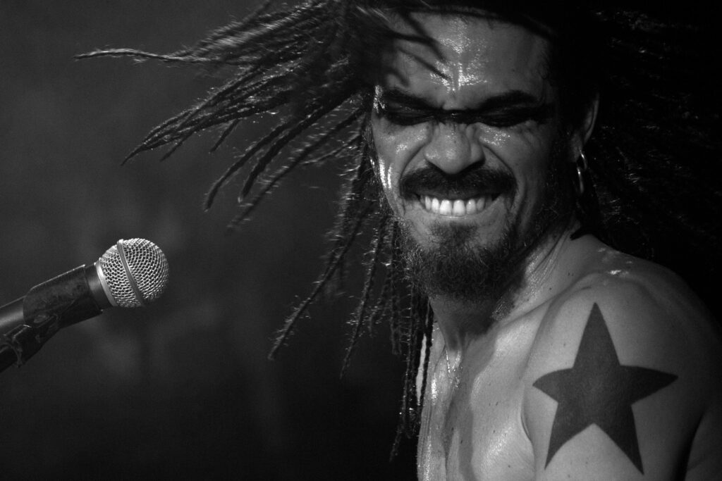 X Alfonso smiling at a microphone, a star tattoo on his shoulder, in a black-and-white photo
