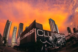 The Club Space building in Miami under an orange sunset sky, high-rises behind