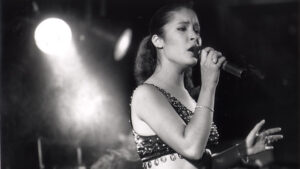Selena Quintanilla singing into a microphone under a spotlight, in a black-and-white photo
