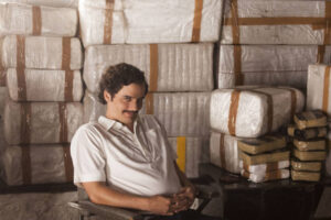 Wagner Moura as Pablo Escobar in Narcos, sitting in front of stacked bales wrapped in plastic