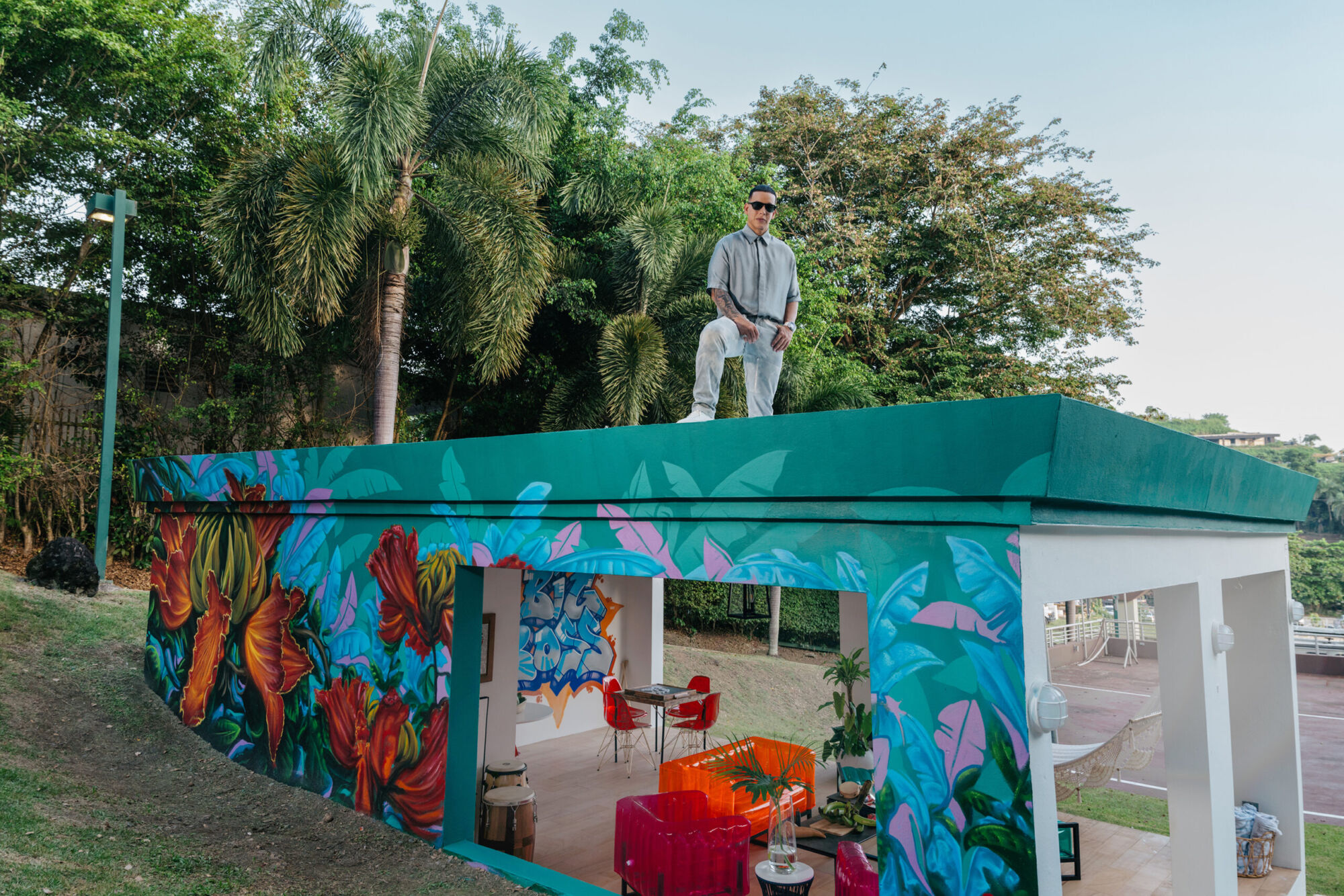 A man standing on the roof of a mural-painted pavilion among palm trees