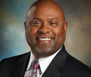 Joe Scantlebury smiling in a dark suit and tie, a studio portrait