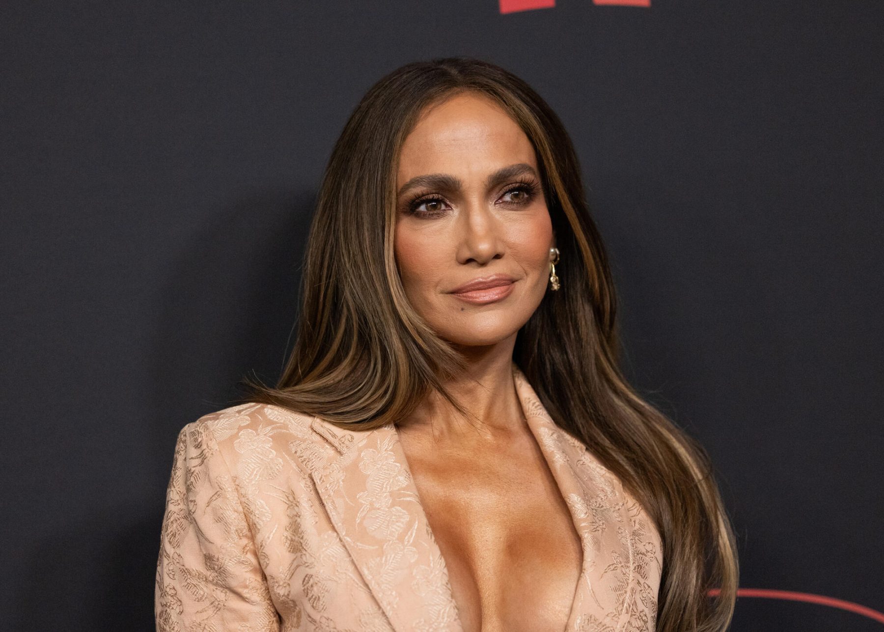 Jennifer Lopez on a red carpet in a blush-pink blazer, hair loose